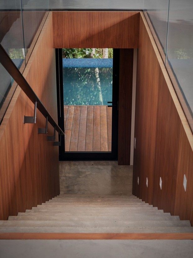 
Một lối cầu thang được xây dựng ở bên trong nhà hướng xuống hồ bơi và không gian ngoài trời

