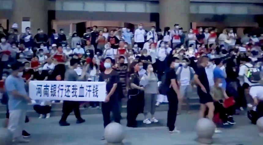 
Đám đông người dân tập trung tại một chi nhánh ở Trịnh Châu của Ngân hàng Trung Quốc, giơ cao biển và hét lớn “trả tiền lại cho chúng tôi”. Ảnh: Bloomberg

